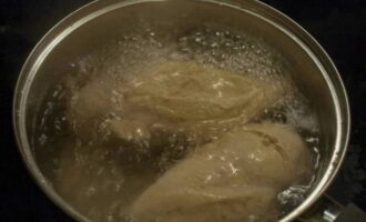 Промываем куриную грудку. Кладем ее в кастрюлю, заливаем водой и доводим до кипения, затем эту воду сливаем. Заливаем курицу чистой водой и отвариваем повторно до готовности.